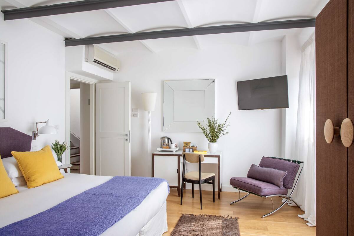 A modern bedroom with a bed, a desk, a chair, and a TV.