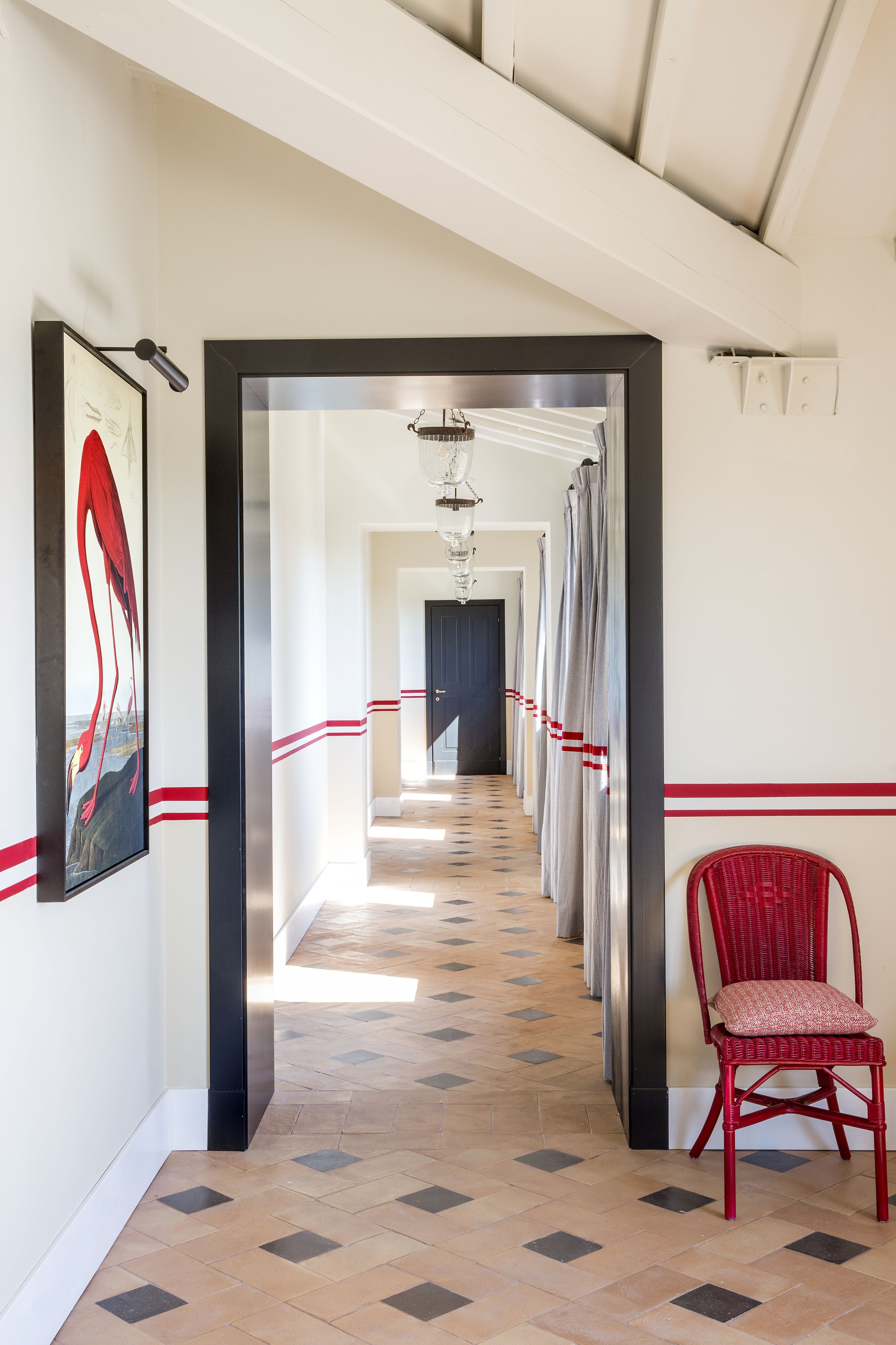 Un pasillo de hotel con suelo de baldosas, una silla roja y un cuadro en la pared.