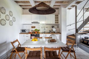 A modern kitchen with white cabinets, a dining table with chairs, a hanging light fixture, and a staircase.