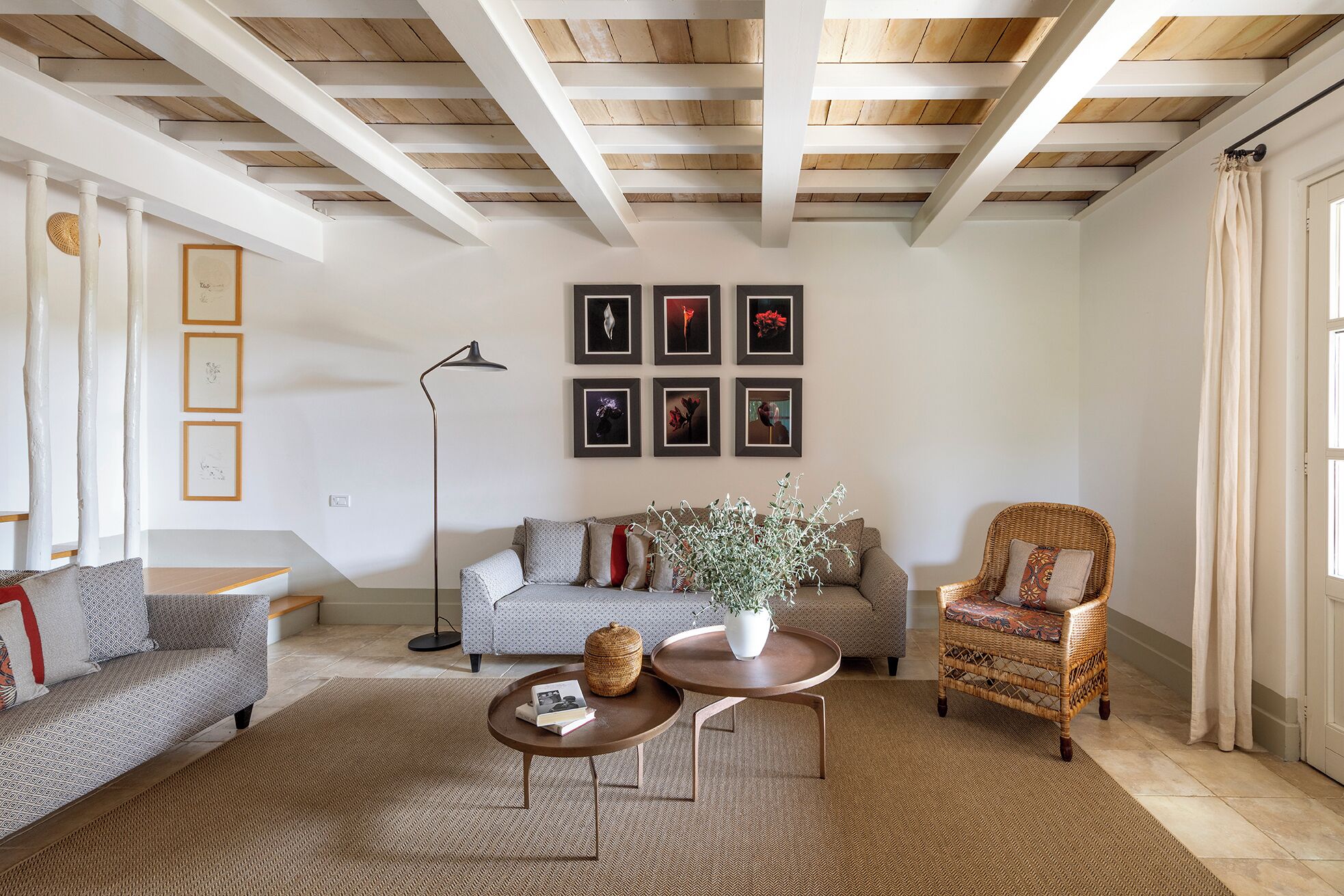 A living room with a high ceiling, exposed wooden beams, a sofa, a chair, a coffee table, and a floor lamp.