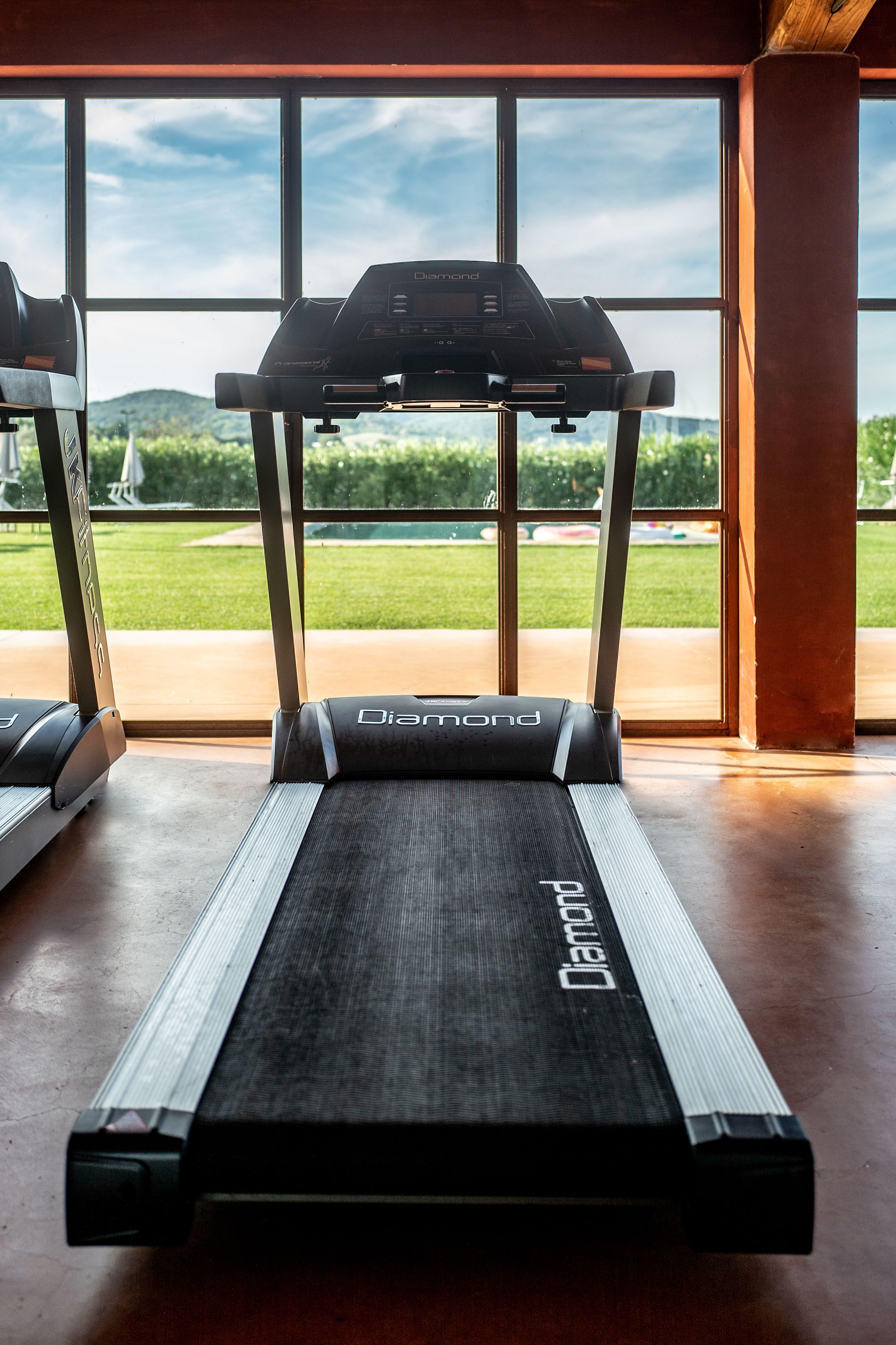 Un tapis de course dans une salle de sport, avec vue sur un paysage verdoyant grâce à de grandes fenêtres.