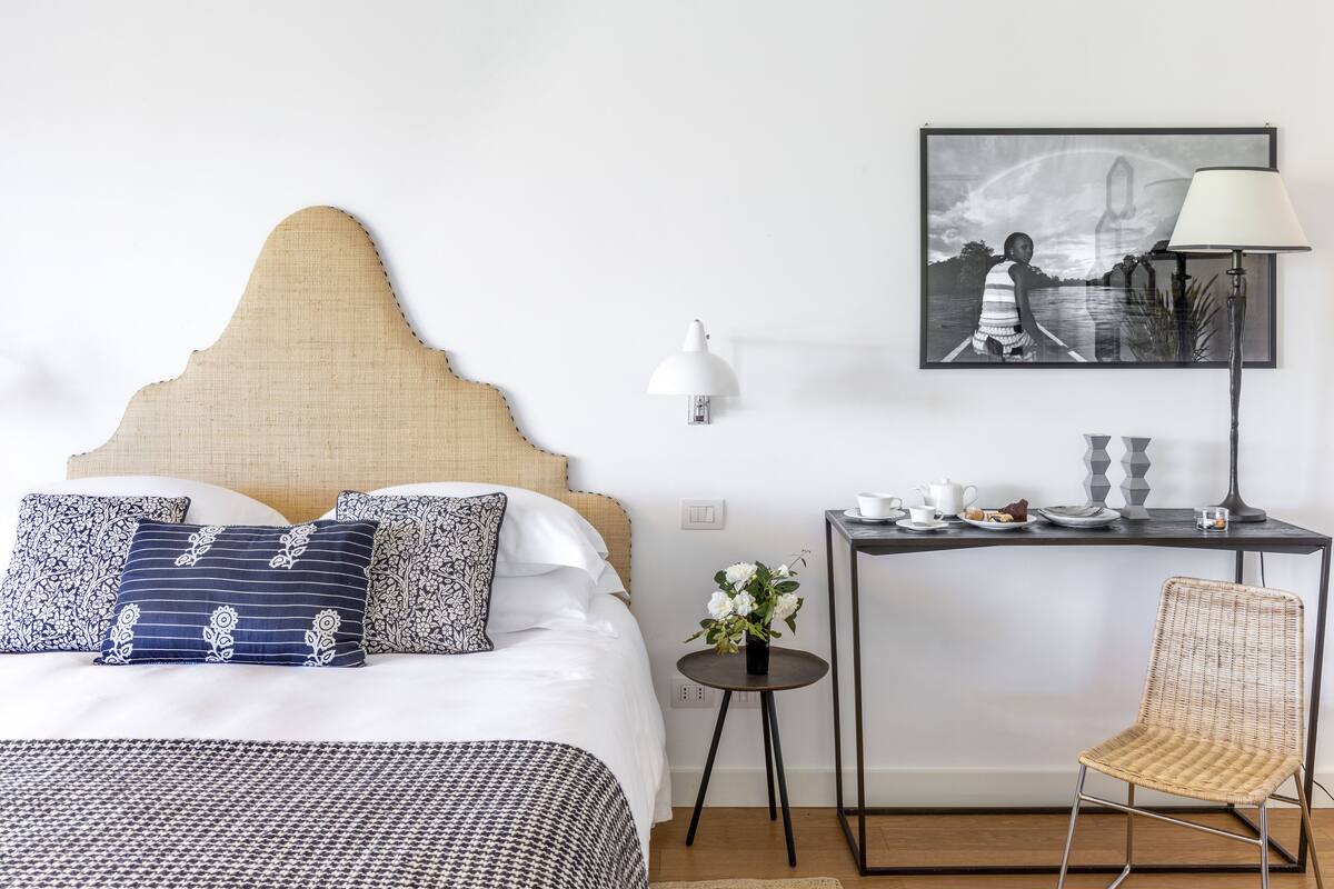 A neatly arranged hotel room with a bed, bedside table, lamp, chair, and a framed picture on the wall.