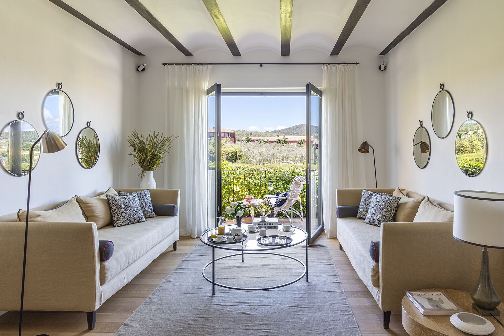 A spacious living room with two sofas, a coffee table, and a view of a garden through large windows.