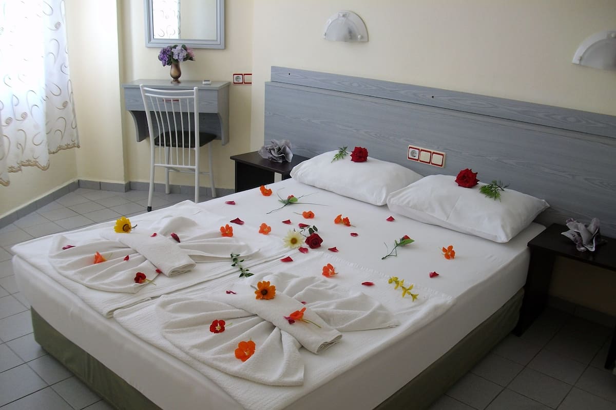 A neatly made bed with floral arrangements and towels, a desk with a chair, and a nightstand with a lamp.
