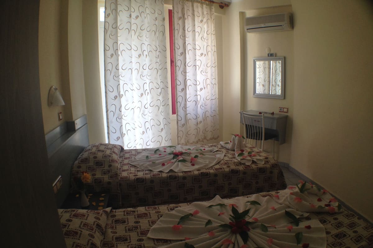 A bedroom with a bed covered in patterned bedding, a bedside table with a lamp, and a window with curtains.