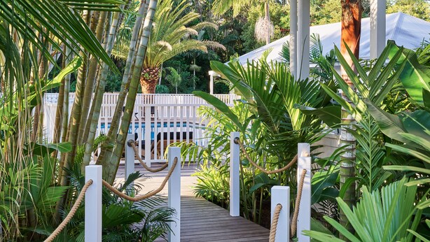 A wooden pathway leading to a white fence with rope barriers, surrounded by lush tropical plants. - Atlantic Byron Bay (Byron Bay)