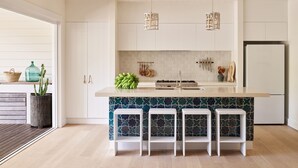 A modern kitchen with white cabinetry, a central island with bar stools, hanging lights, and a backsplash with a geometric pattern. - Atlantic Byron Bay (Byron Bay)
