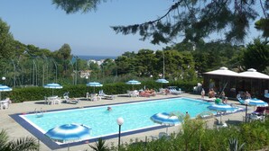 Une piscine entourée d’arbres, avec des chaises longues et des parasols, et offrant une vue sur la mer.