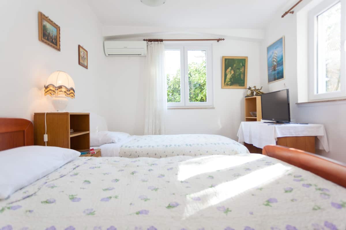 A bedroom with two beds, a TV, a lamp, and a window with curtains.