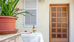 A terrace with a table set for two, a potted plant, a bottle of wine, and a wooden door with glass panels. - Dubrovnik Center Apartments (Dubrovnik)