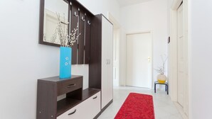 A hallway with a red carpet, a dark wooden cabinet with drawers, a blue vase with branches, and a white door at the end. - Dubrovnik Center Apartments (Dubrovnik)
