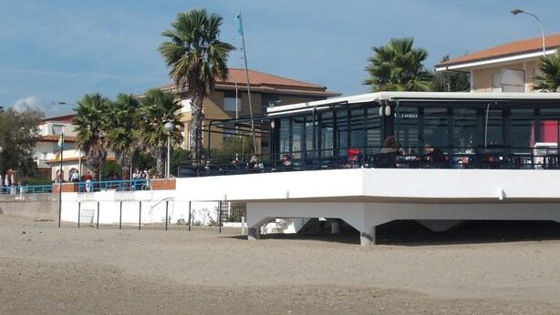 A bus station with a covered waiting area and a building in the background. - Hotel San Carlo (Terracina)