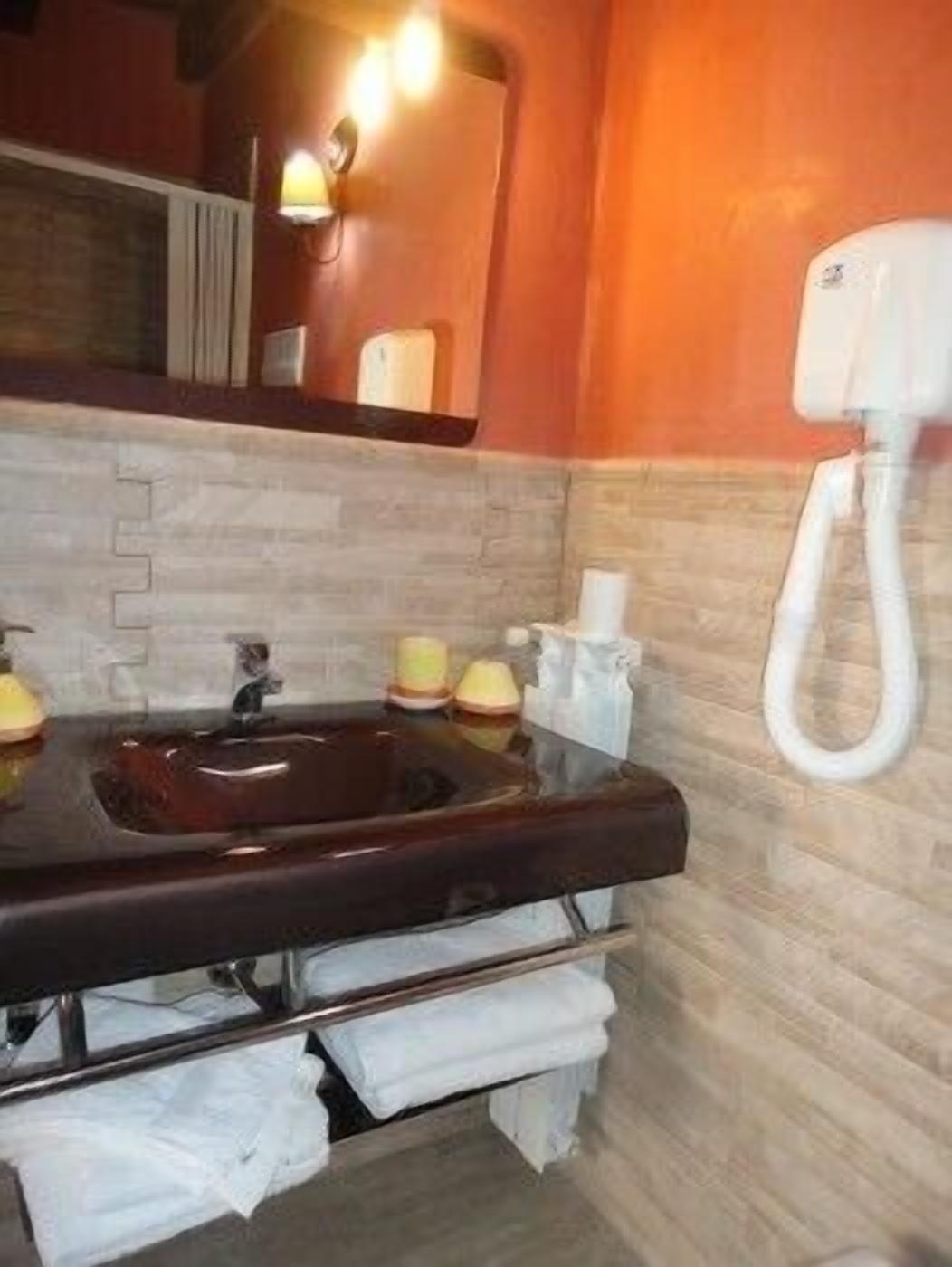 Un baño con un lavamanos marrón oscuro, toallas blancas y un secamanos.