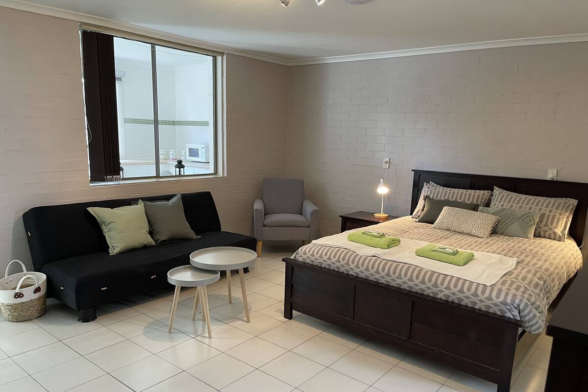 A bedroom with a bed, a sofa, a chair, a small table, and a window.