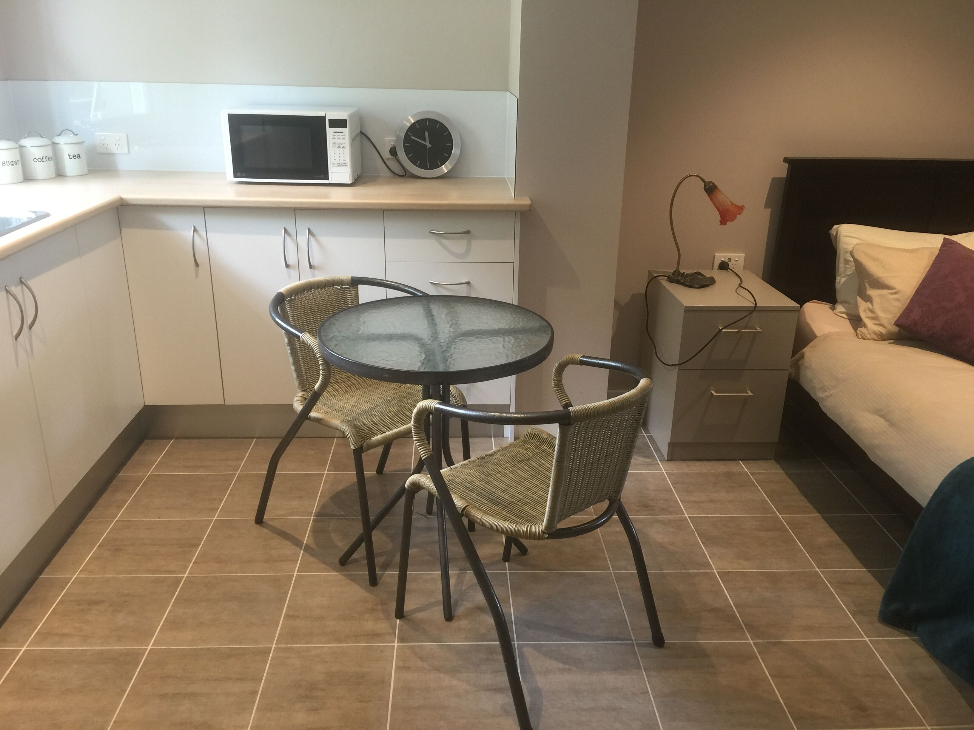 Une cuisine compacte équipée d’un four à micro-ondes, d’une horloge et d’une petite table à manger avec des chaises en osier.