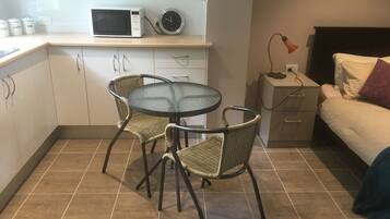 Una cocina compacta con microondas, un reloj y una pequeña mesa de comedor con sillas de mimbre.