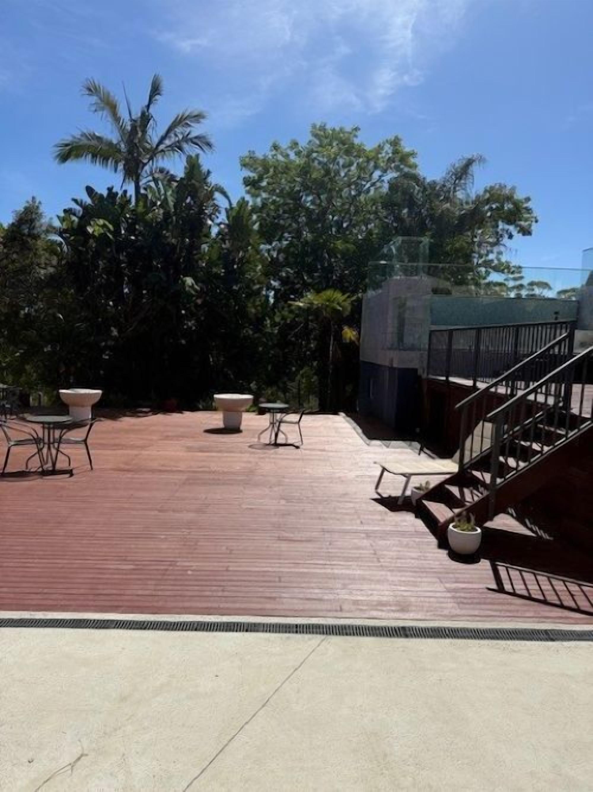 Terraza en la azotea con mobiliario exterior, una escalera y follaje circundante.