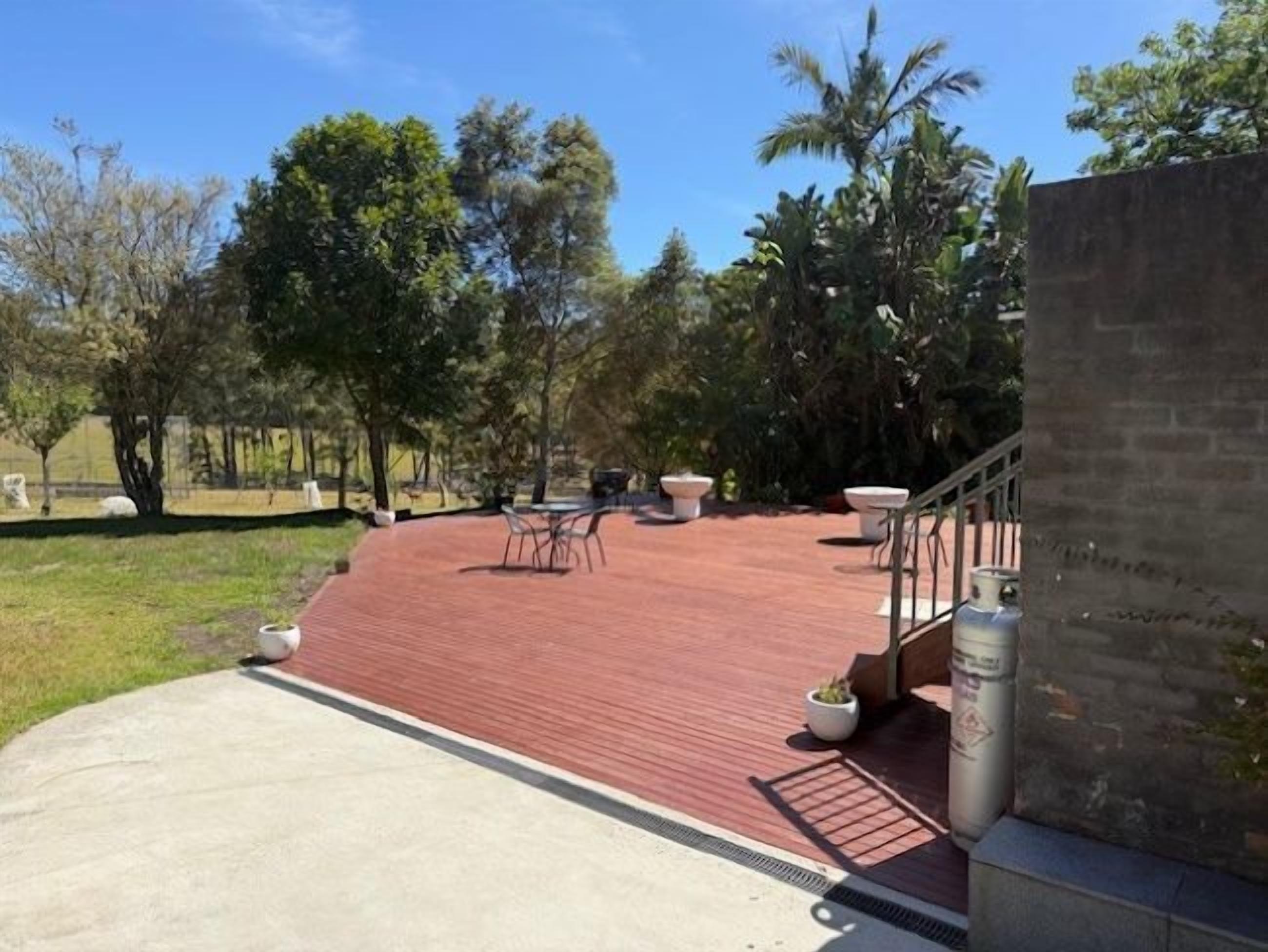 A covered outdoor patio with a red floor, outdoor furniture, and a staircase leading to an upper level.