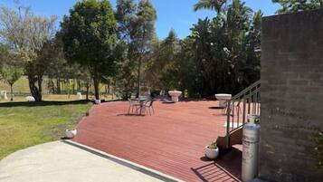 A covered outdoor patio with a red floor, outdoor furniture, and a staircase leading to an upper level.