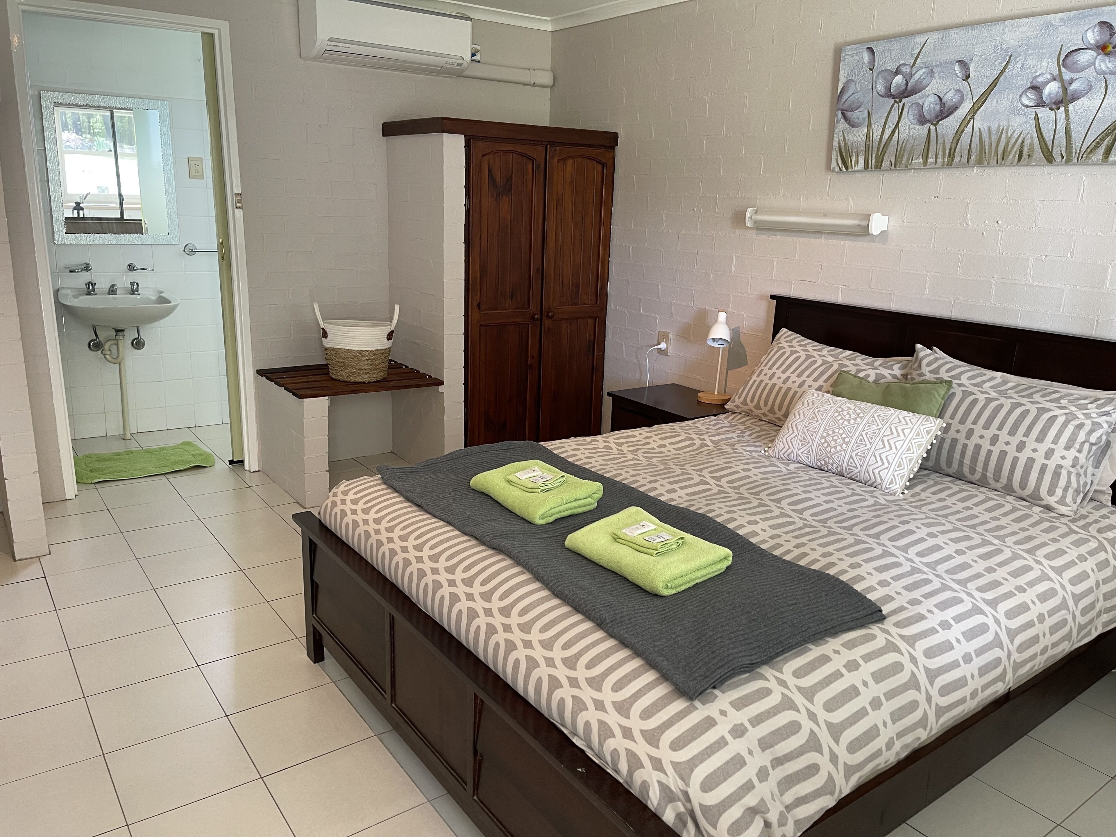A bedroom with a bed, a nightstand, a lamp, a dresser, a mirror, and a bathroom with a sink.