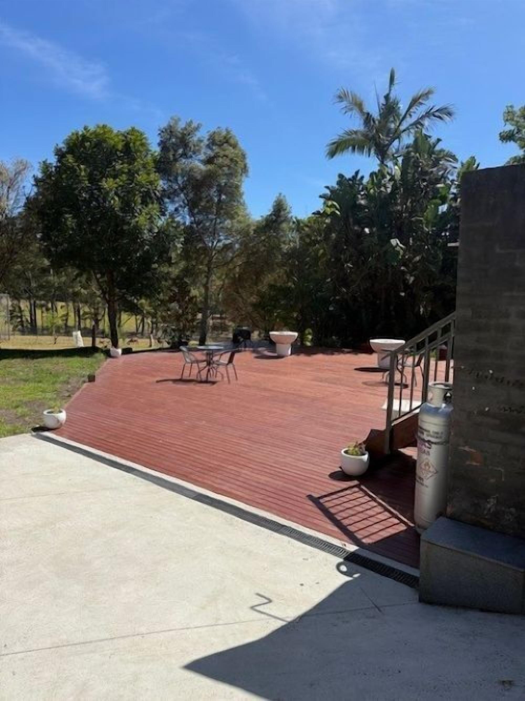 A paved outdoor area with a red surface, surrounded by trees and a stone wall.