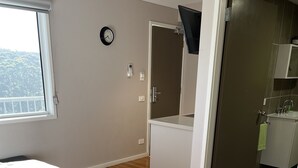 A bedroom with a bed, a window, a door leading to a bathroom, and a clock on the wall.