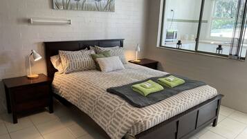 A neatly arranged bedroom with a patterned bedspread, two pillows, a bedside lamp, and a window with a view of the outdoors.