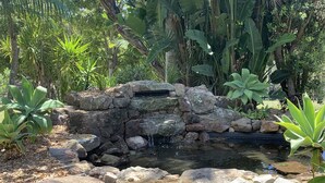 A small waterfall in a garden with a stone structure, surrounded by various plants.