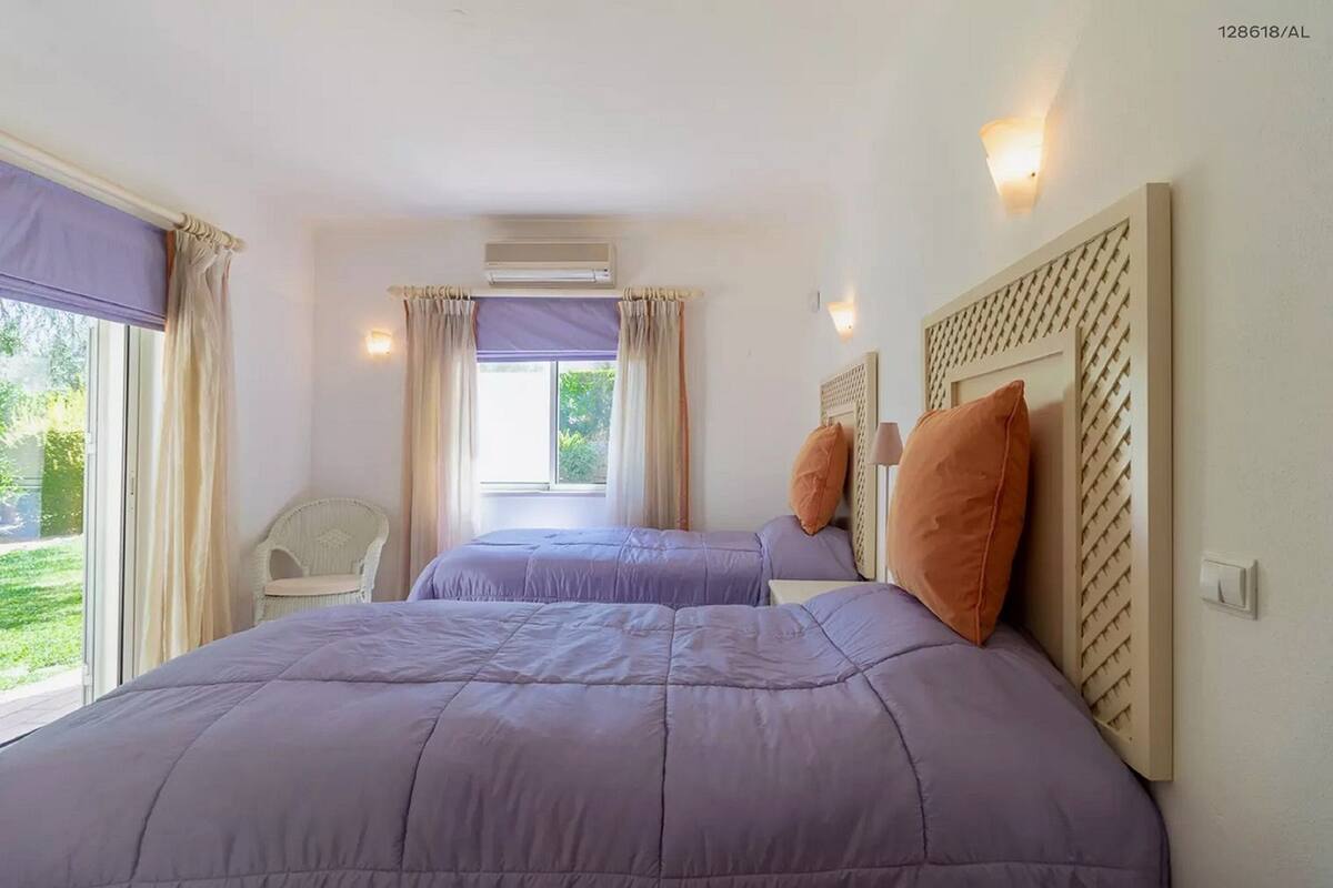 A bedroom with two beds, a chair, and a window with curtains.