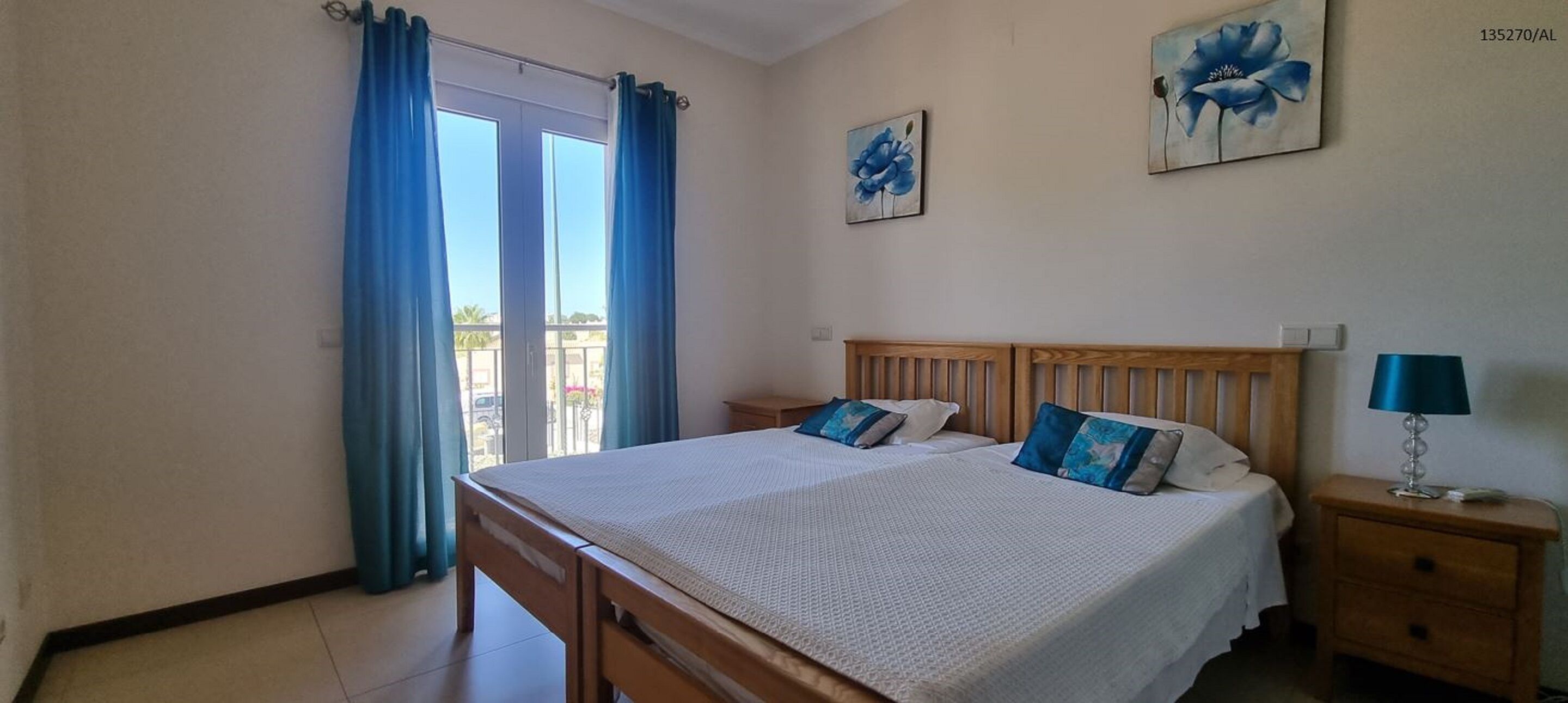 A bedroom with a bed, nightstands, a lamp, and a view through a window with curtains.