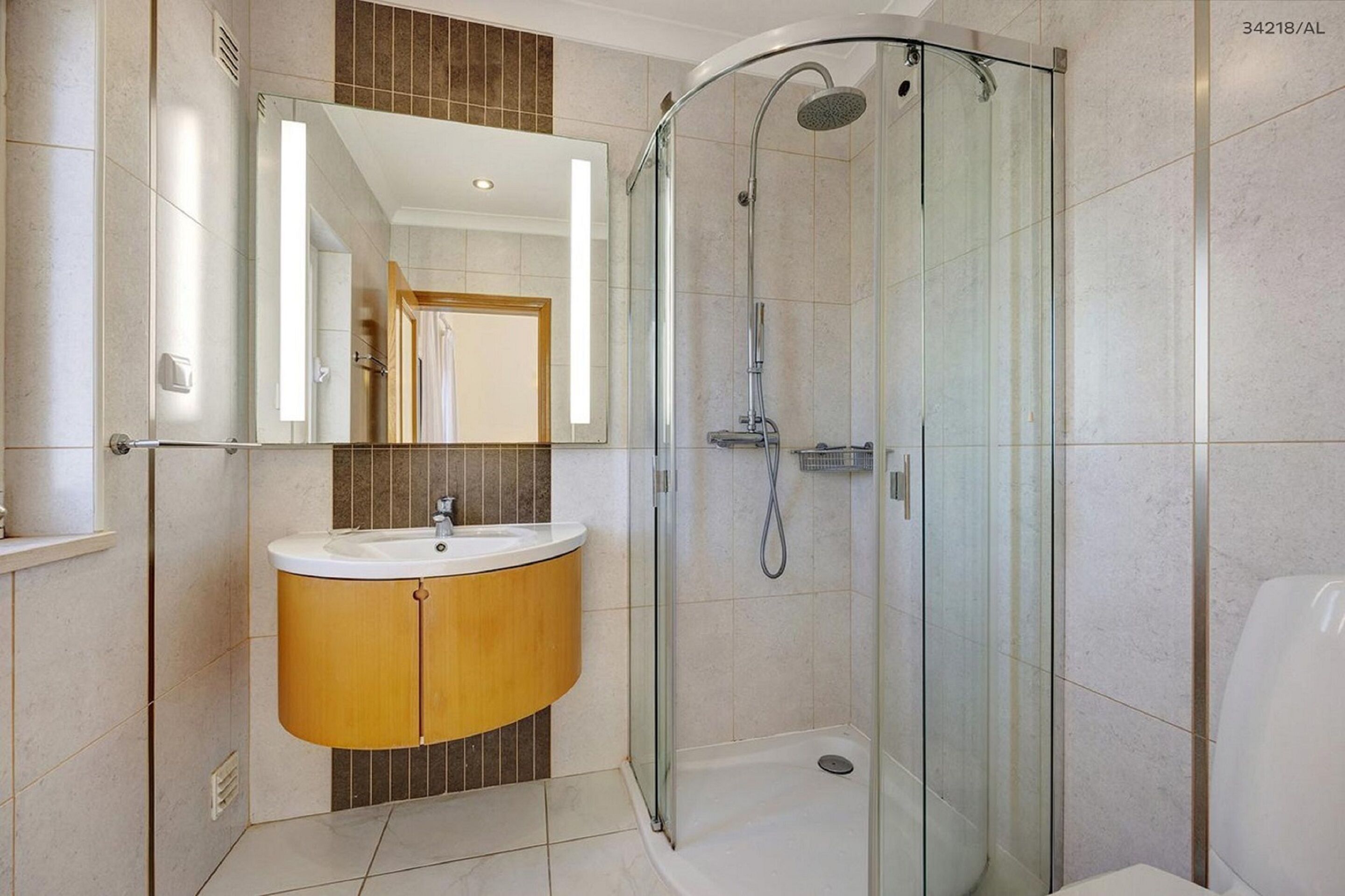 Ein modernes Badezimmer mit einer gläsernen Dusche, einem Holzkosmetikschrank und einem großen Spiegel.
