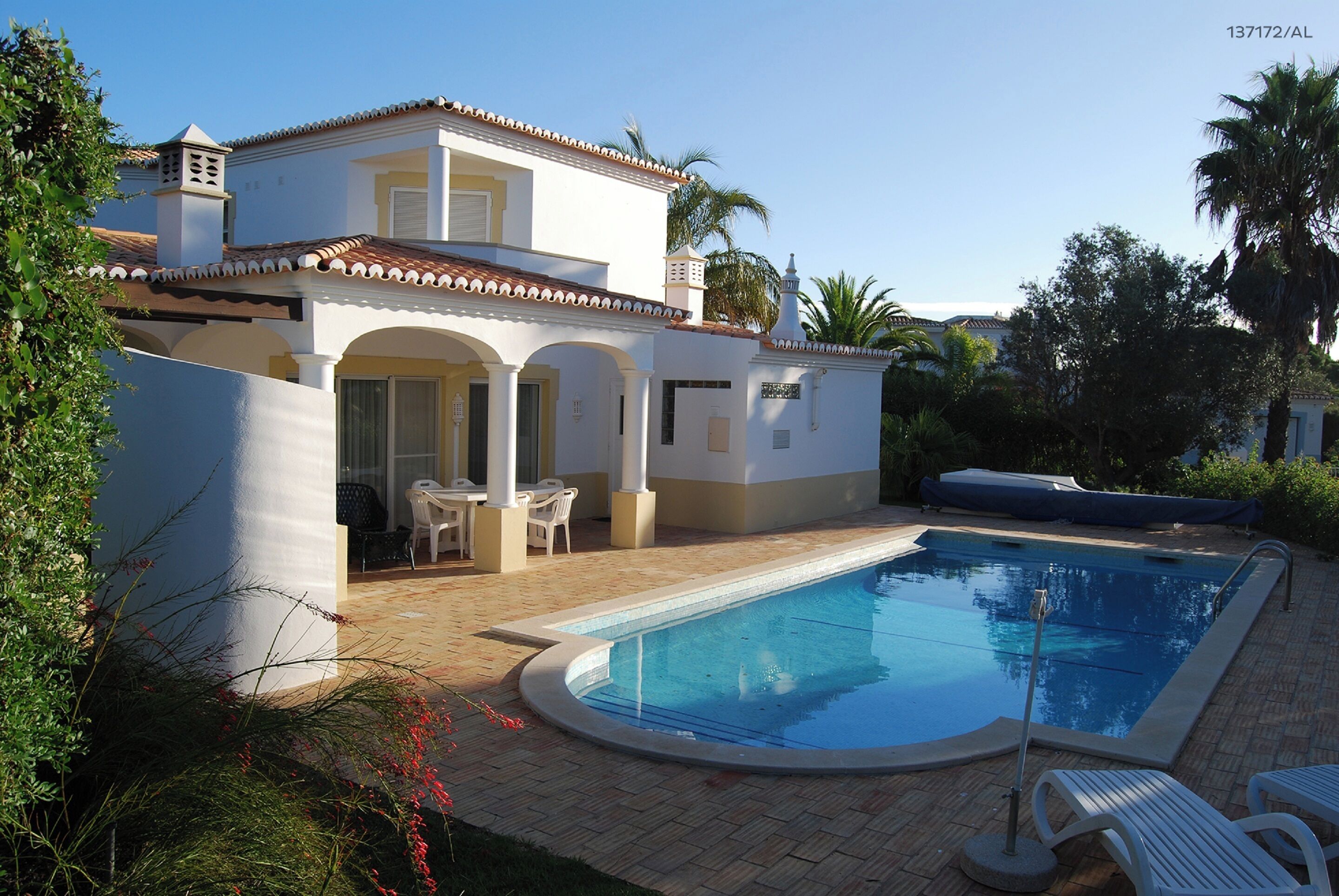 A two-story house with a swimming pool, outdoor furniture, and a garden.