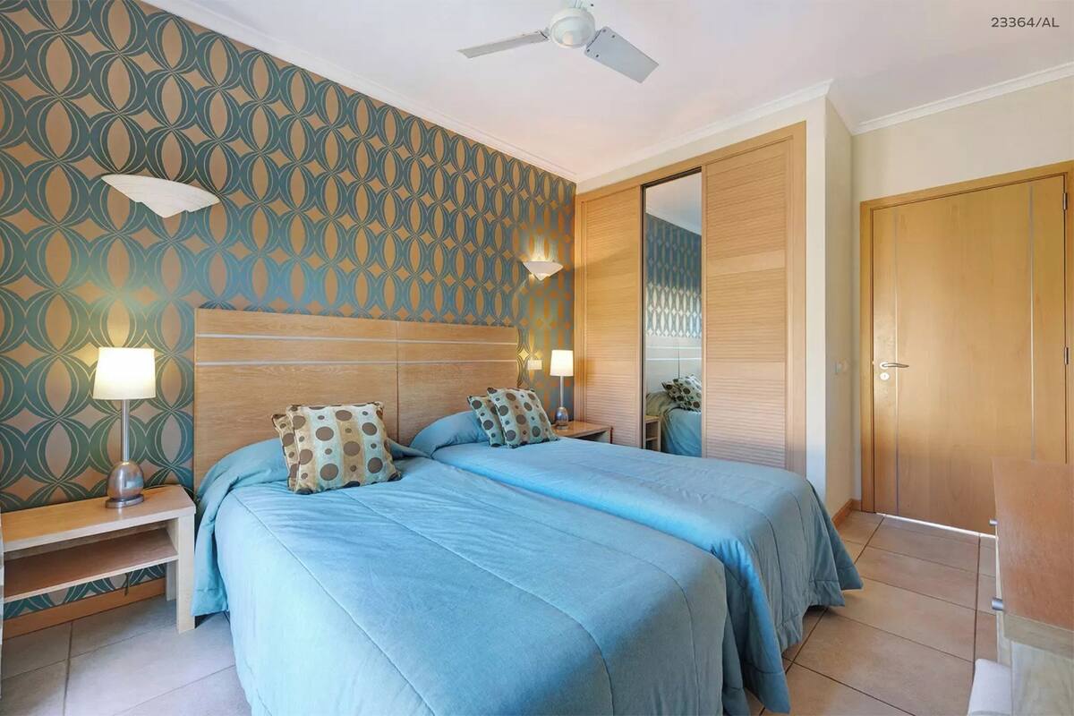 A bedroom with two beds, a ceiling fan, and a wooden wardrobe.