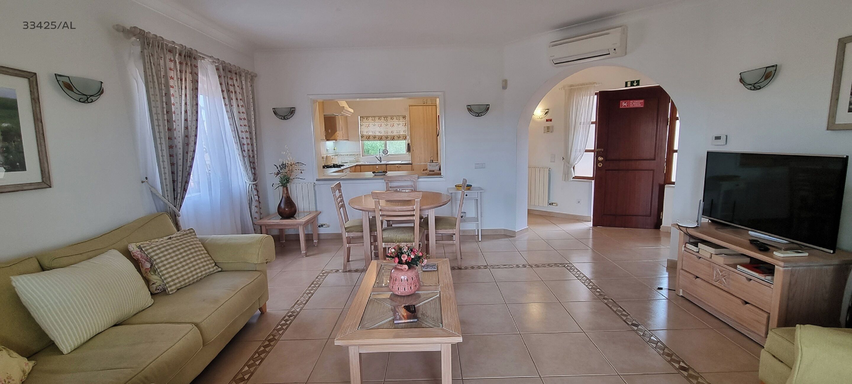 Una sala de estar con sofá, mesa de centro, mueble para televisión y una cocina al fondo.