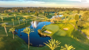 Un parcours de golf avec un étang, des palmiers et une vue lointaine sur la ville.