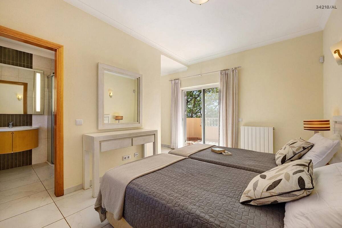 A hotel room with two beds, a bathroom with a mirror, and a balcony with curtains.