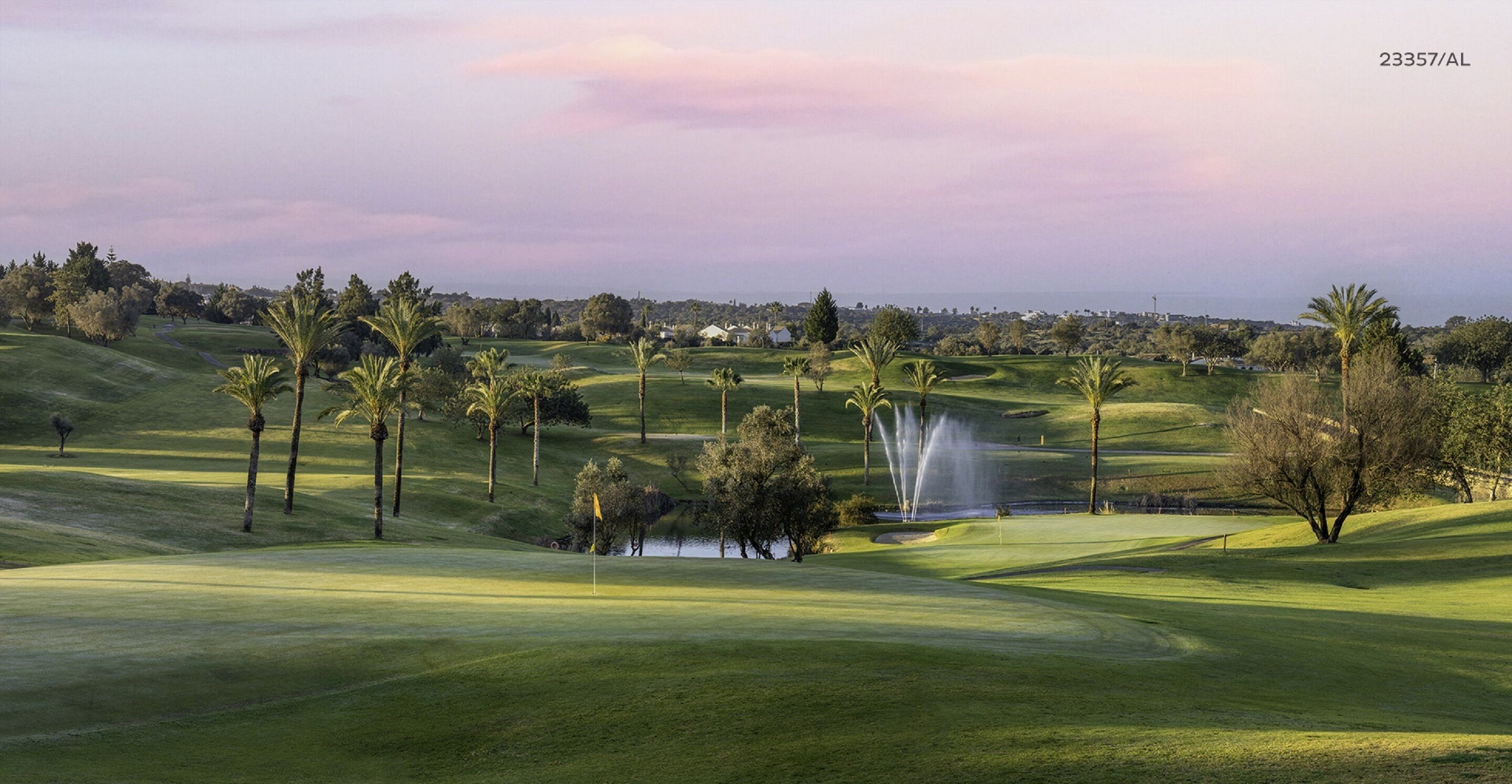 A golf course with a water fountain, palm trees, and a flag on the green.