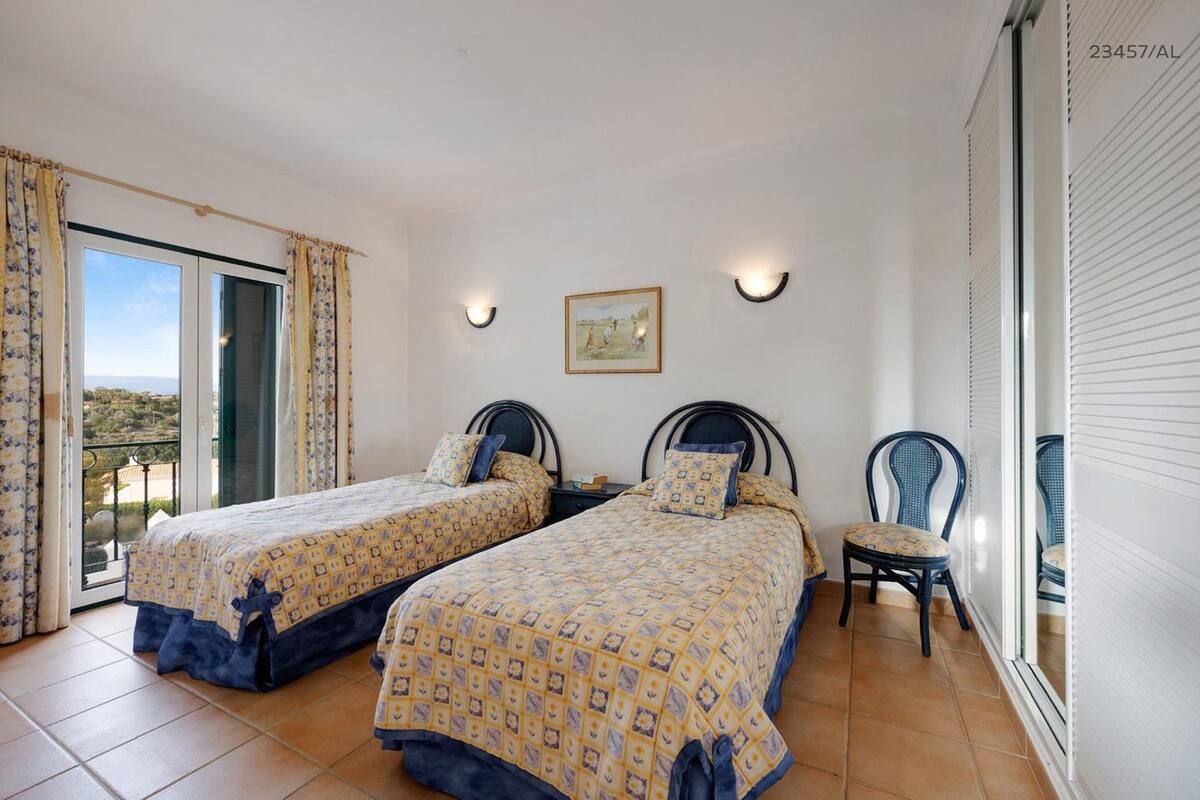 A bedroom with two beds, a chair, and a balcony.