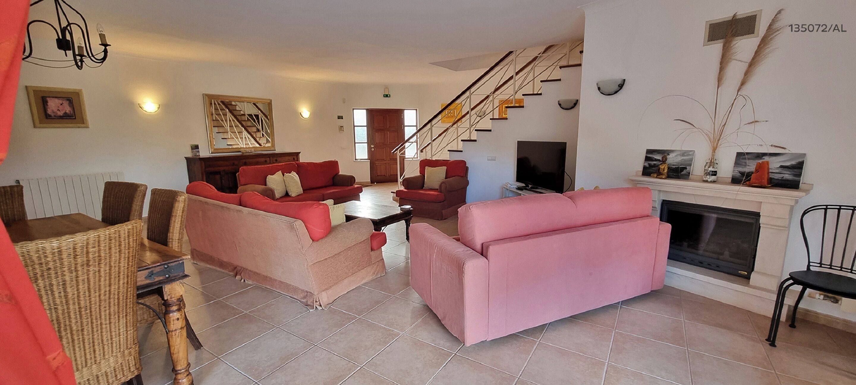 Un amplio salón con chimenea, una escalera y un comedor con mobiliario de mimbre.