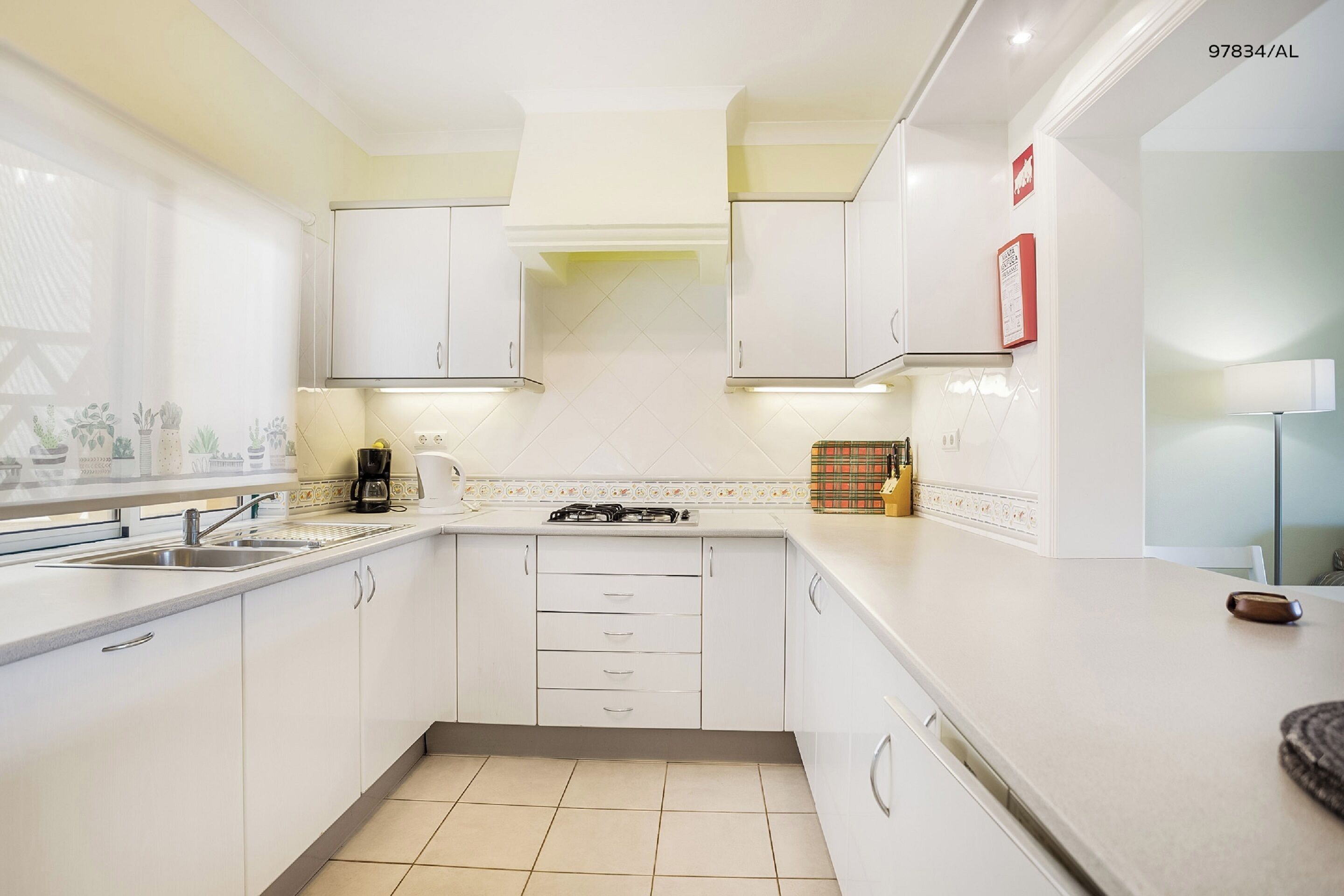 Une cuisine moderne avec des meubles blancs, une cuisinière à gaz et une machine à café.