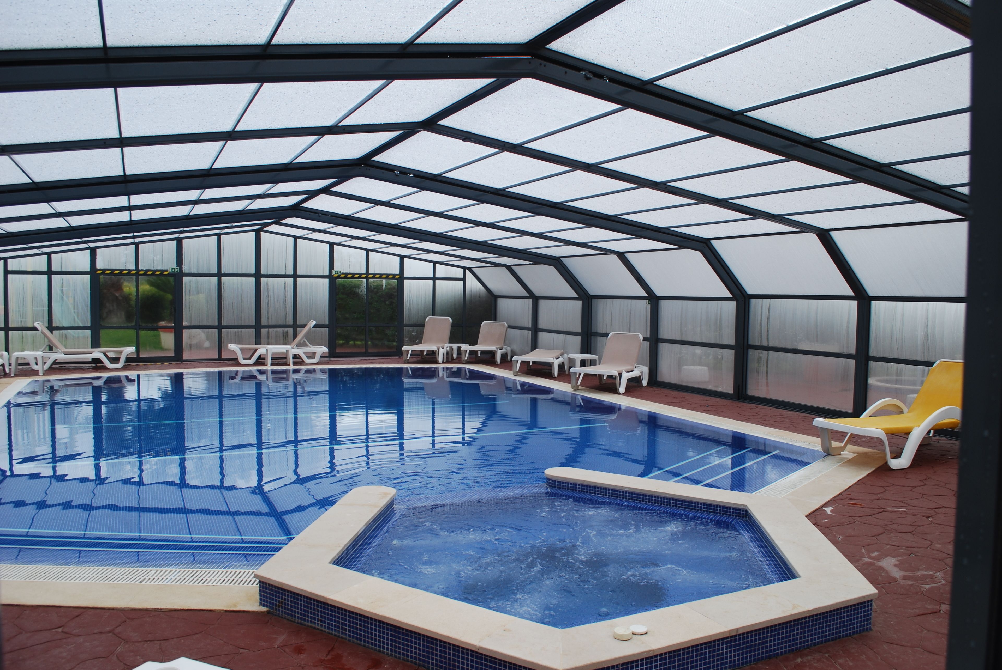 Una piscina cubierta con varias pistas de natación, rodeada de sillones de descanso y un recinto de cristal.