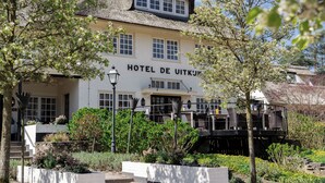 Un hotel con fachada blanca y techo de paja, rodeado de exuberante vegetación y un jardín bien cuidado.