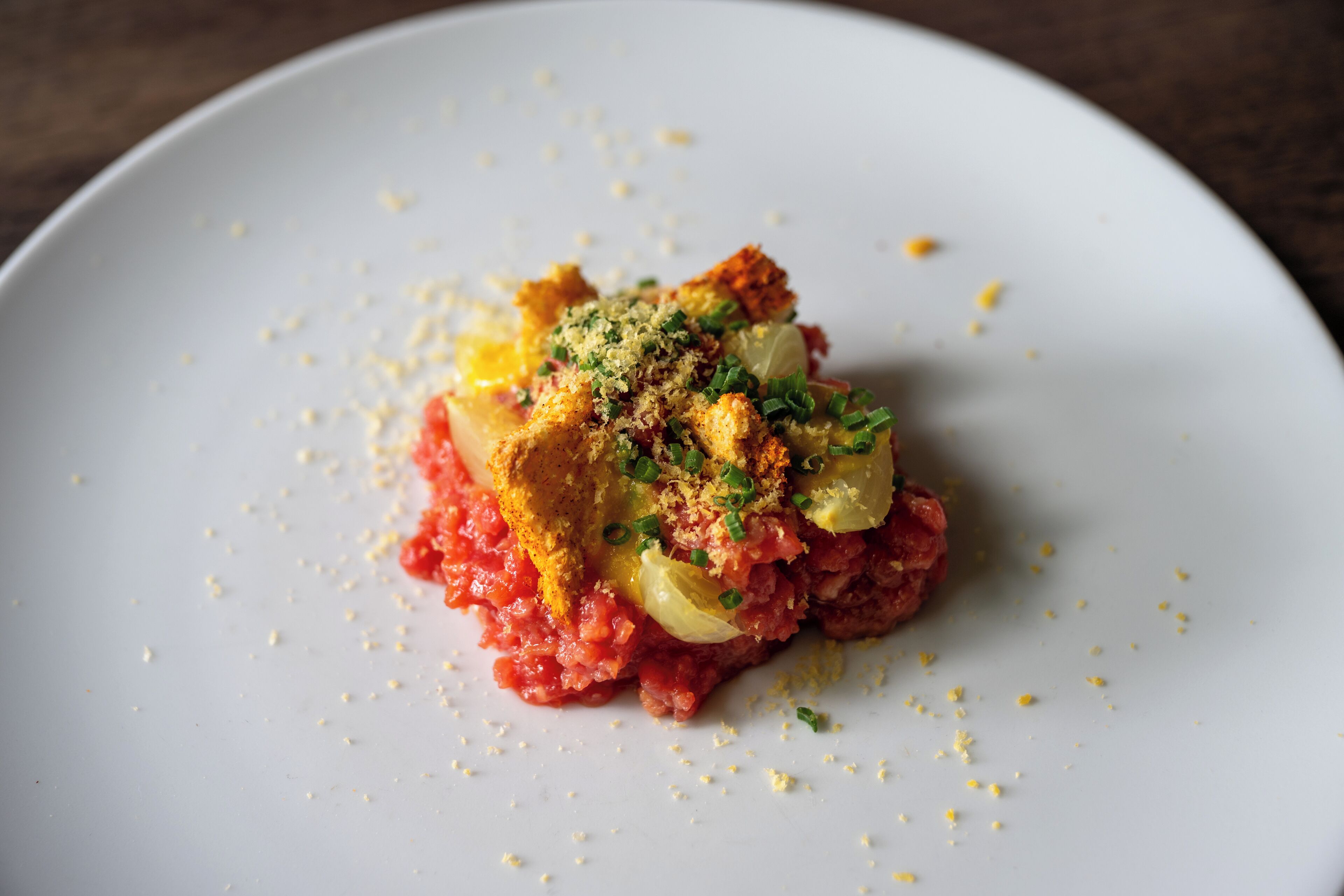 A white plate with a food item topped with breadcrumbs and green herbs.