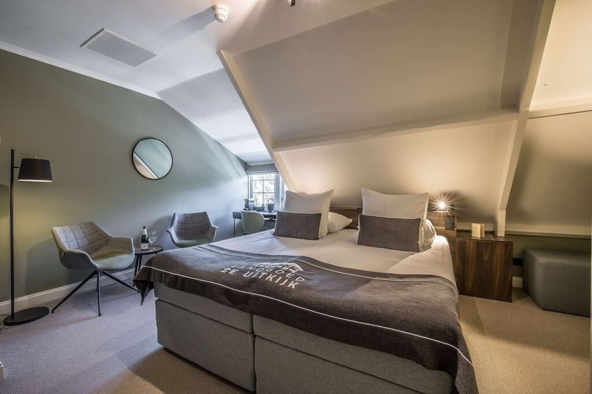 A modern bedroom with a bed, two chairs, a bedside table, and a mirror.