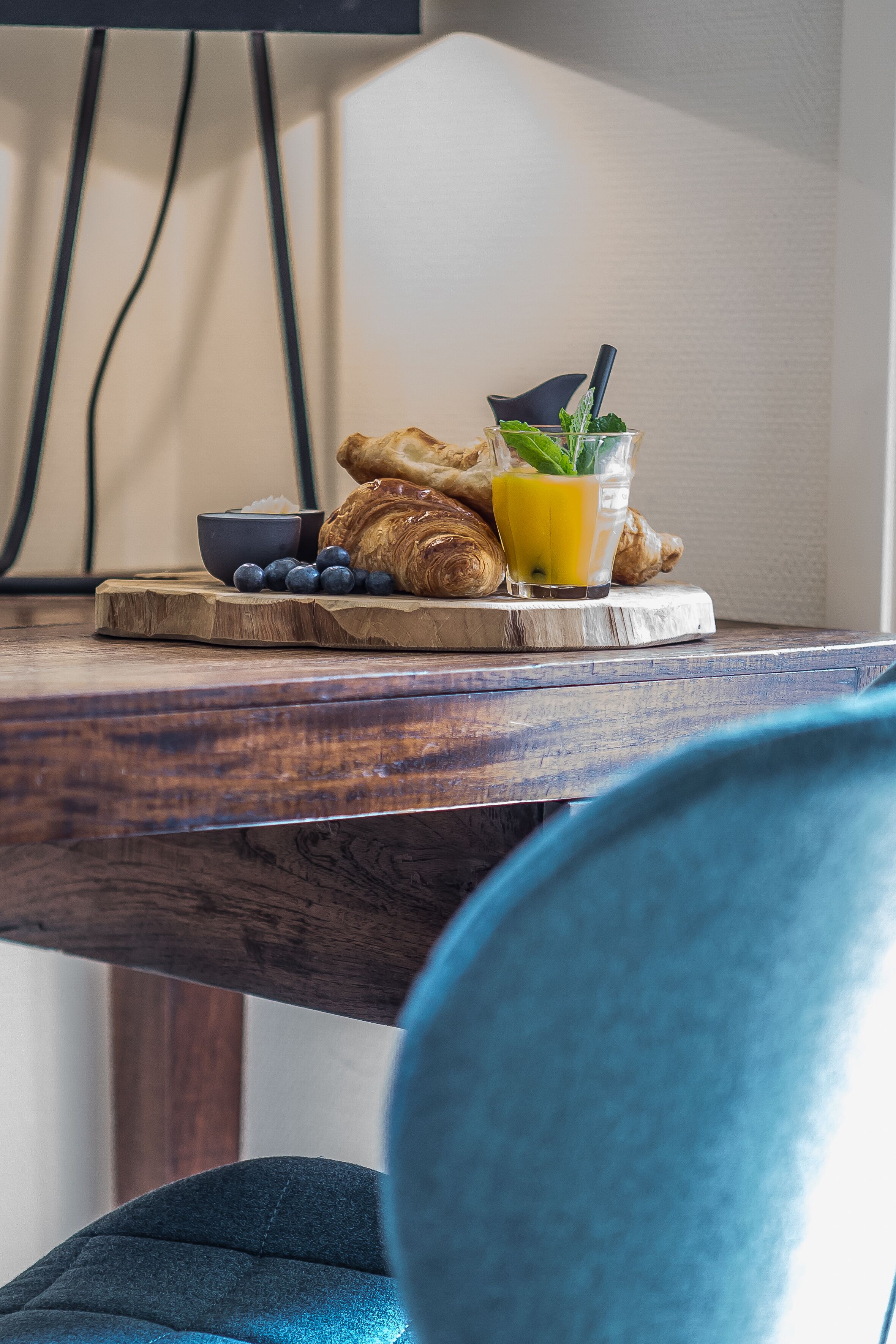 Un desayuno con cruasanes, arándanos y un vaso de jugo de naranja sobre una tabla de madera.