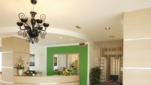 Zona de recepción de hotel con mostrador curvo, una pared de acento verde, un sofá y una araña.