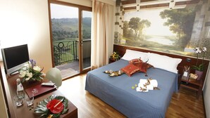 Una habitación de hotel con cama, escritorio con computadora, ventana con vista al campo y un cuadro en la pared.