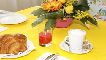 Una escena de desayuno con croissants, una taza de café y un arreglo floral sobre una mesa amarilla.