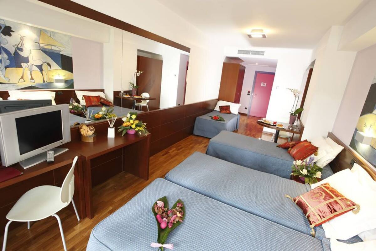 A hotel room with two beds, a desk with a TV, and a chair.