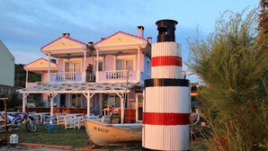 Un edificio costero con balcón, un faro y un barco llamado 'YANAZIP' en primer plano.